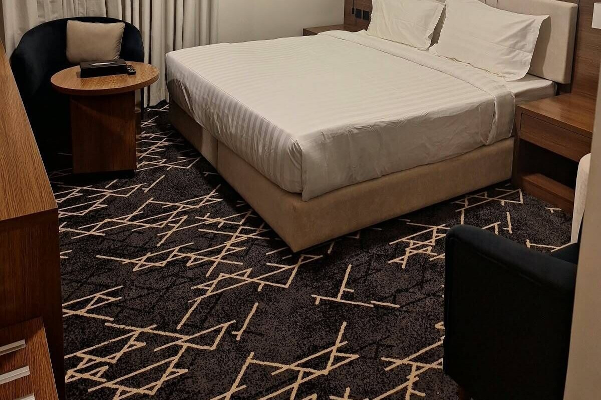 Een hotelkamer met een bed, een stoel, een nachtkastje, een lamp en een raam met gordijnen.