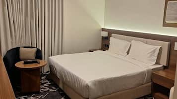 A hotel room with a bed, a chair, a nightstand, a lamp, and a window with curtains.