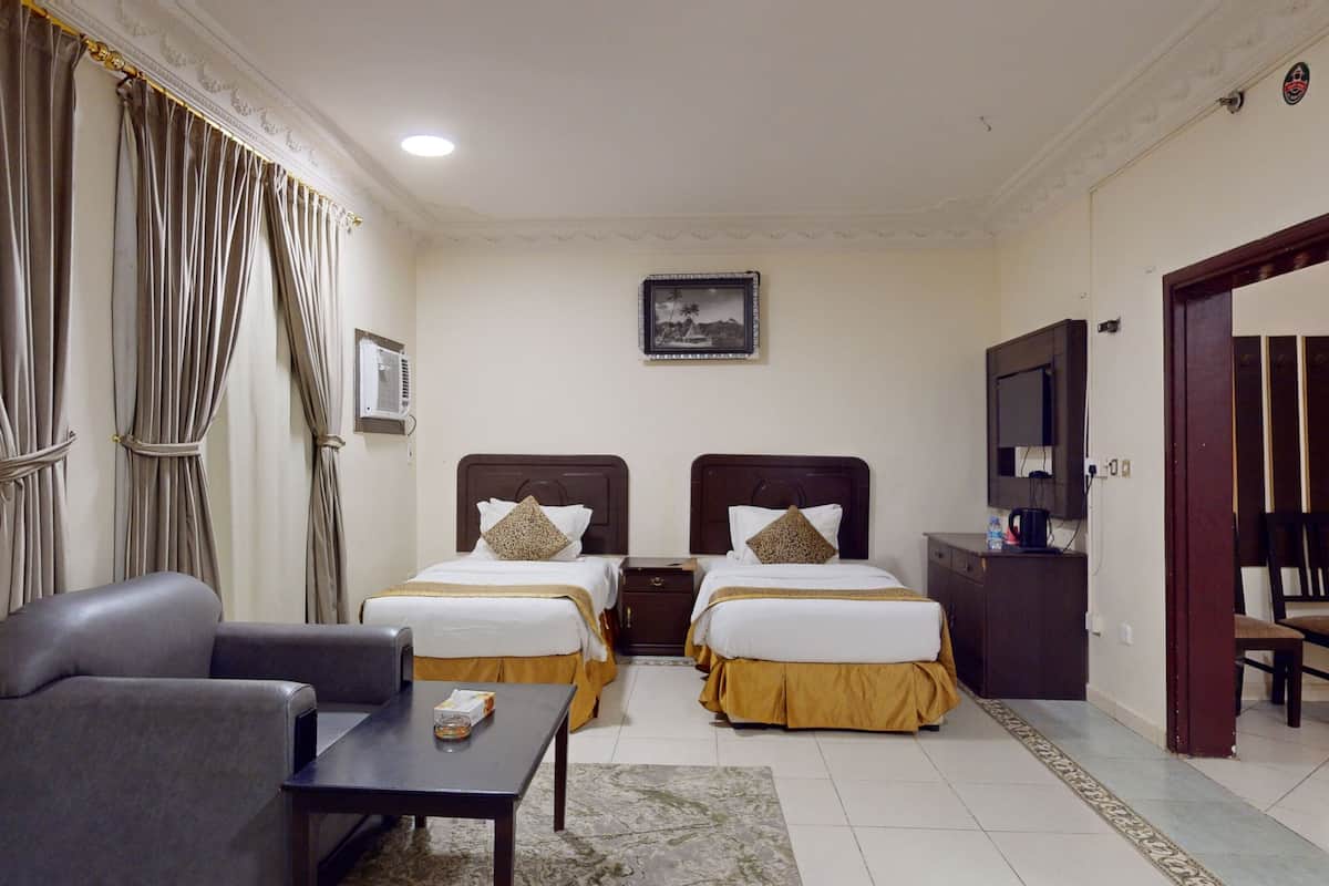 Habitación de hotel con dos camas, un sofá, una mesa, un televisor y un cuadro en la pared.