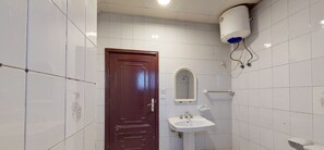 Ein Badezimmer mit weißen Fliesen, einer Holztür, einem weißen Waschbecken, einem Spiegel und einer Toilette.
