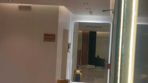 Un pasillo con una puerta que da a una habitación, un letrero en la pared y una pequeña mesa con un teléfono.
