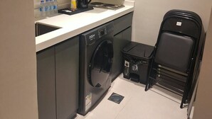 Una cocina compacta con lavadora, cafetera y una pila de sillas negras.