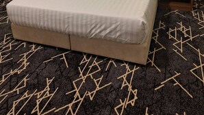 Una habitación de hotel con una cama grande, dos mesitas de noche y una alfombra estampada.