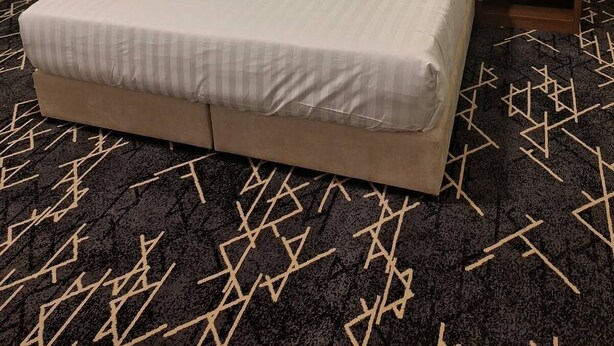 Una habitación de hotel con una cama grande, dos mesitas de noche y una alfombra estampada.