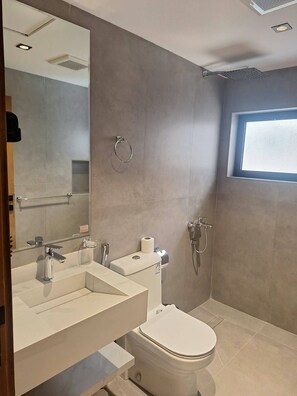 Een moderne badkamer met toilet, hygiëneschuimer en een grote spiegel.