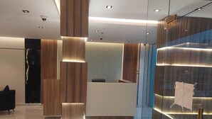 A modern reception area with a wooden reception desk, a glass partition, and a seating area with a black sofa. - Wahat Al Madinah Hotel Apartments (Madinah)