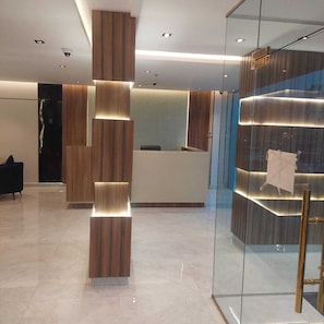 Een moderne receptie met een houten balie, een glazen scheidingswand en een zithoek met een zwarte bank.