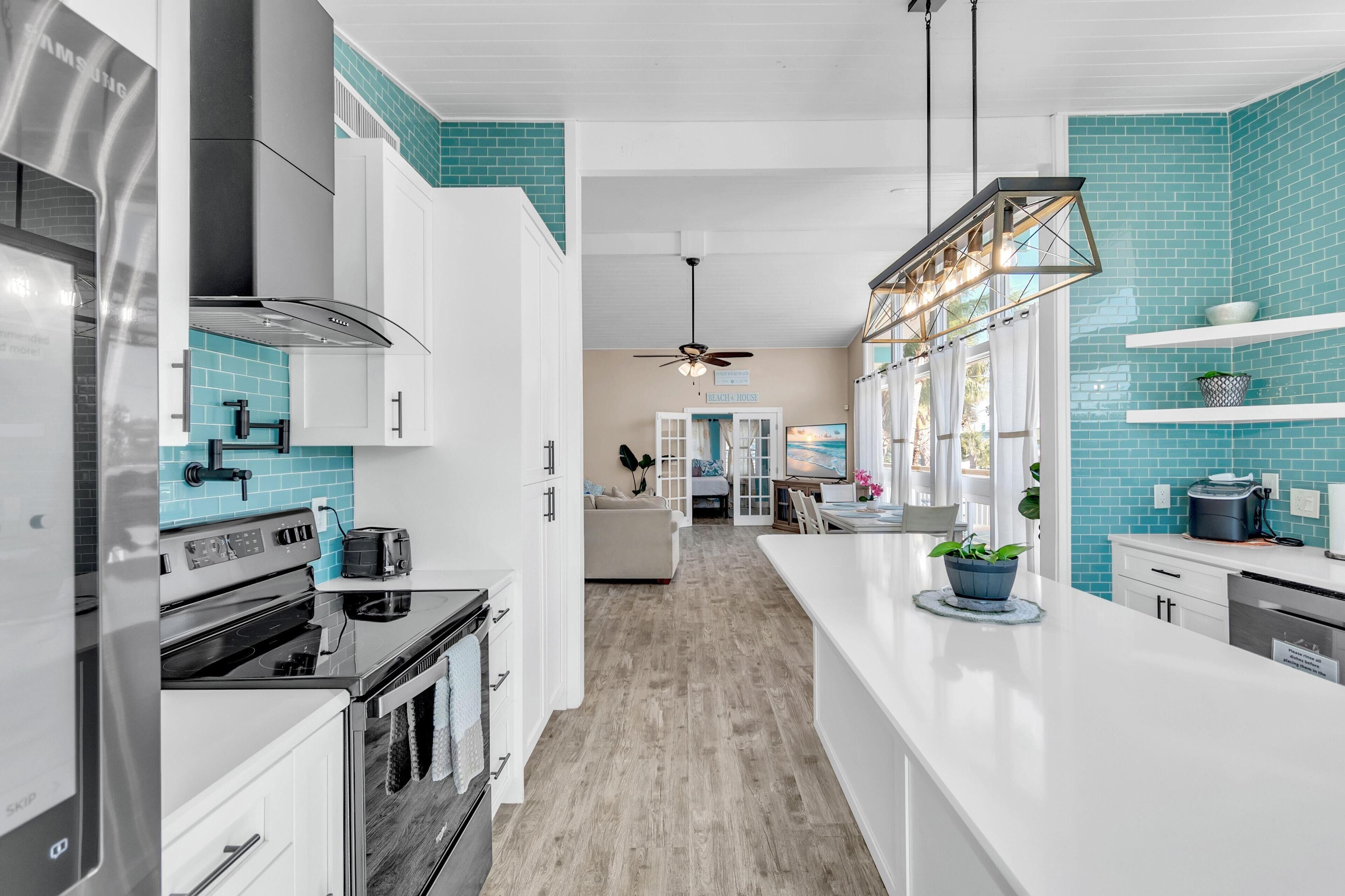 A modern kitchen with white cabinets, a stainless steel range hood, and a blue-tiled backsplash.