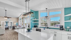 A modern kitchen with white cabinetry, a large island, and blue-tiled walls. - Bates Avenue House (Indian Rocks Beach)