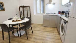 A compact kitchen with a dining area, including a round table, chairs, a cabinet, a washing machine, and a window. - Devalù Politeama elegante appartamento al centro (palermo)