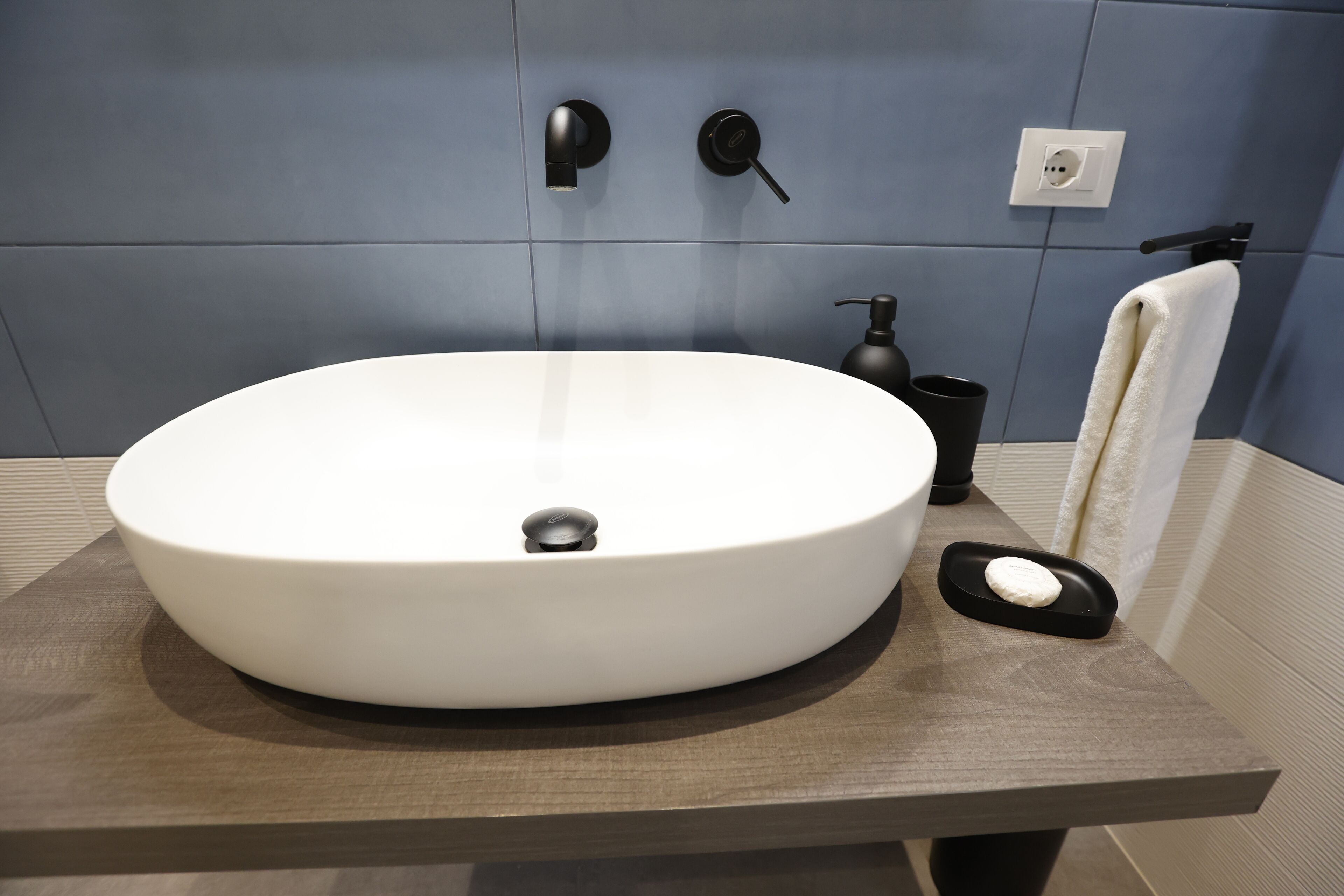 A modern bathroom with a large white sink, a black faucet, a soap dispenser, and a towel rack.