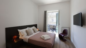 A modern hotel bedroom with a large bed, a bedside table with a lamp, a chair, and a TV mounted on the wall. - Devalù Politeama elegante appartamento al centro (palermo)