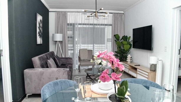 Una sala de estar moderna con una mesa de comedor de vidrio, un sofá y un televisor montado en la pared.