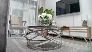 Una sala de estar moderna con una mesa de centro de vidrio, un sillón cómodo, un aparador de madera y un televisor de pantalla plana grande montado en la pared.