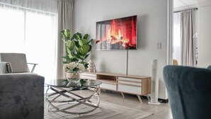 Una sala de estar moderna con una mesa de centro de vidrio, un sofá, un televisor montado en la pared y un amplio ventanal con cortinas.