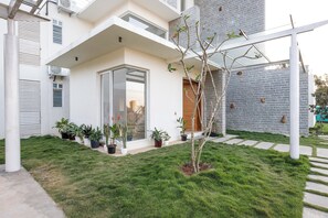 A modern house with a glass door entrance, a small garden with potted plants, and a brick wall. - Golf View Home by Stayjade (Hosur)