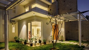 A modern house with a glass entryway, a covered patio, and a brick exterior. - Golf View Home by Stayjade (Hosur)
