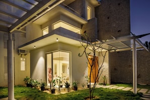 A modern house with a glass entryway, a covered patio, and a brick exterior. - Golf View Home by Stayjade (Hosur)