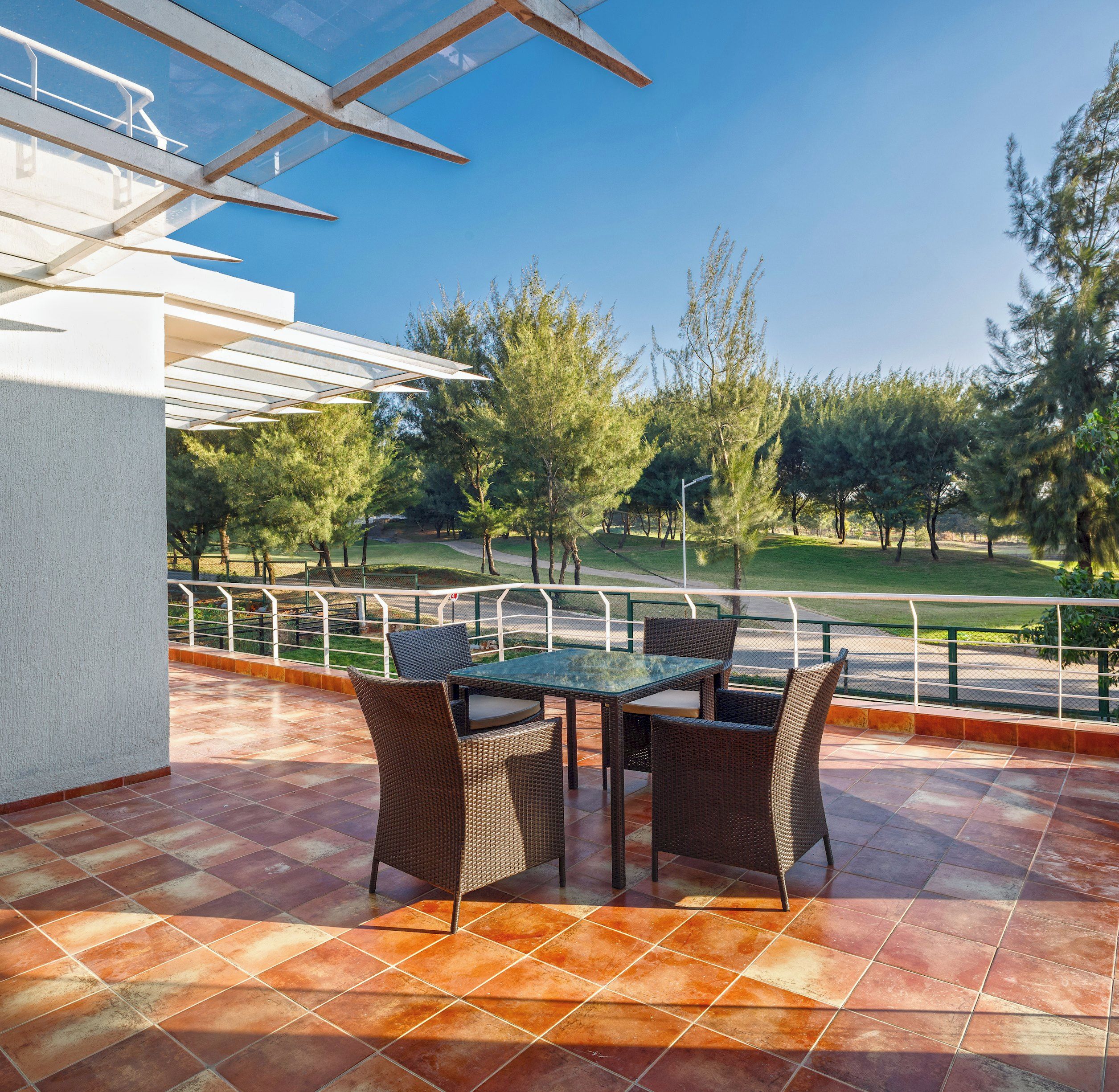 An outdoor patio with a table and chairs, a pergola, and a view of a park with trees and a road.