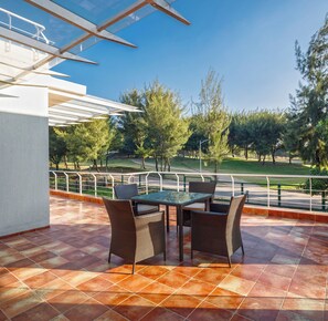 An outdoor patio with a table and chairs, a pergola, and a view of a park with trees and a road. - Golf View Home by Stayjade (Hosur)