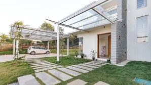 A modern house with a covered patio, a car parked outside, and a well-maintained lawn. - Golf View Home by Stayjade (Hosur)