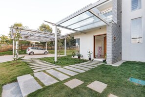 A modern house with a covered patio, a car parked outside, and a well-maintained lawn. - Golf View Home by Stayjade (Hosur)