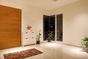 A modern interior with a wooden door, a white cabinet, and two potted plants. - Golf View Home by Stayjade (Hosur)