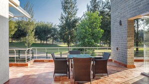 An outdoor patio with a table and chairs, a brick wall, and a view of a golf course. - Golf View Home by Stayjade (Hosur)