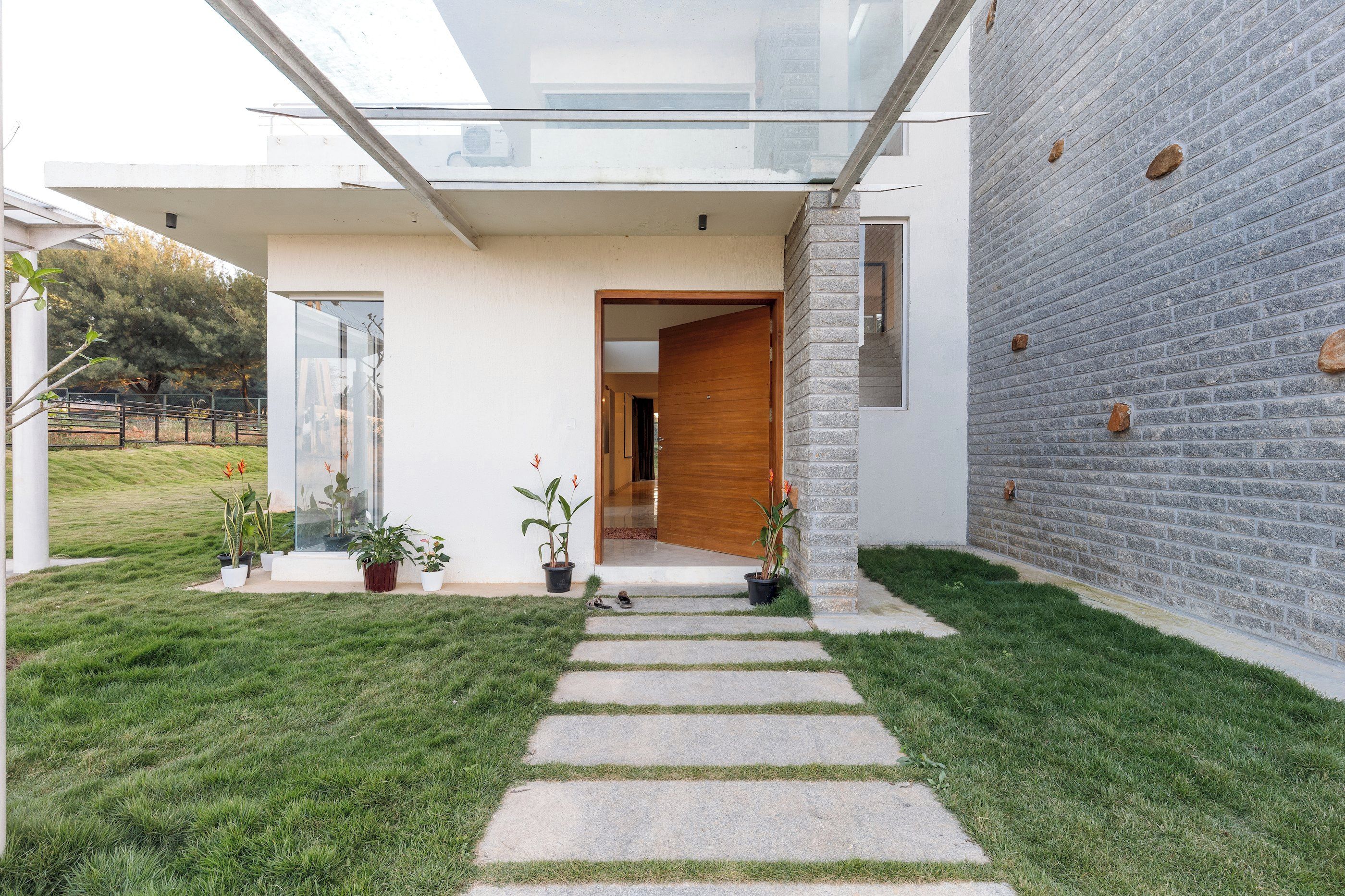 A modern house with a glass extension, a stone wall, and a well-maintained lawn.
