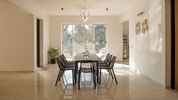 A modern dining room with a rectangular table and six chairs, large windows, and a potted plant.