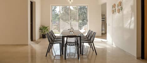 A modern dining room with a rectangular table and six chairs, large windows, and a potted plant.