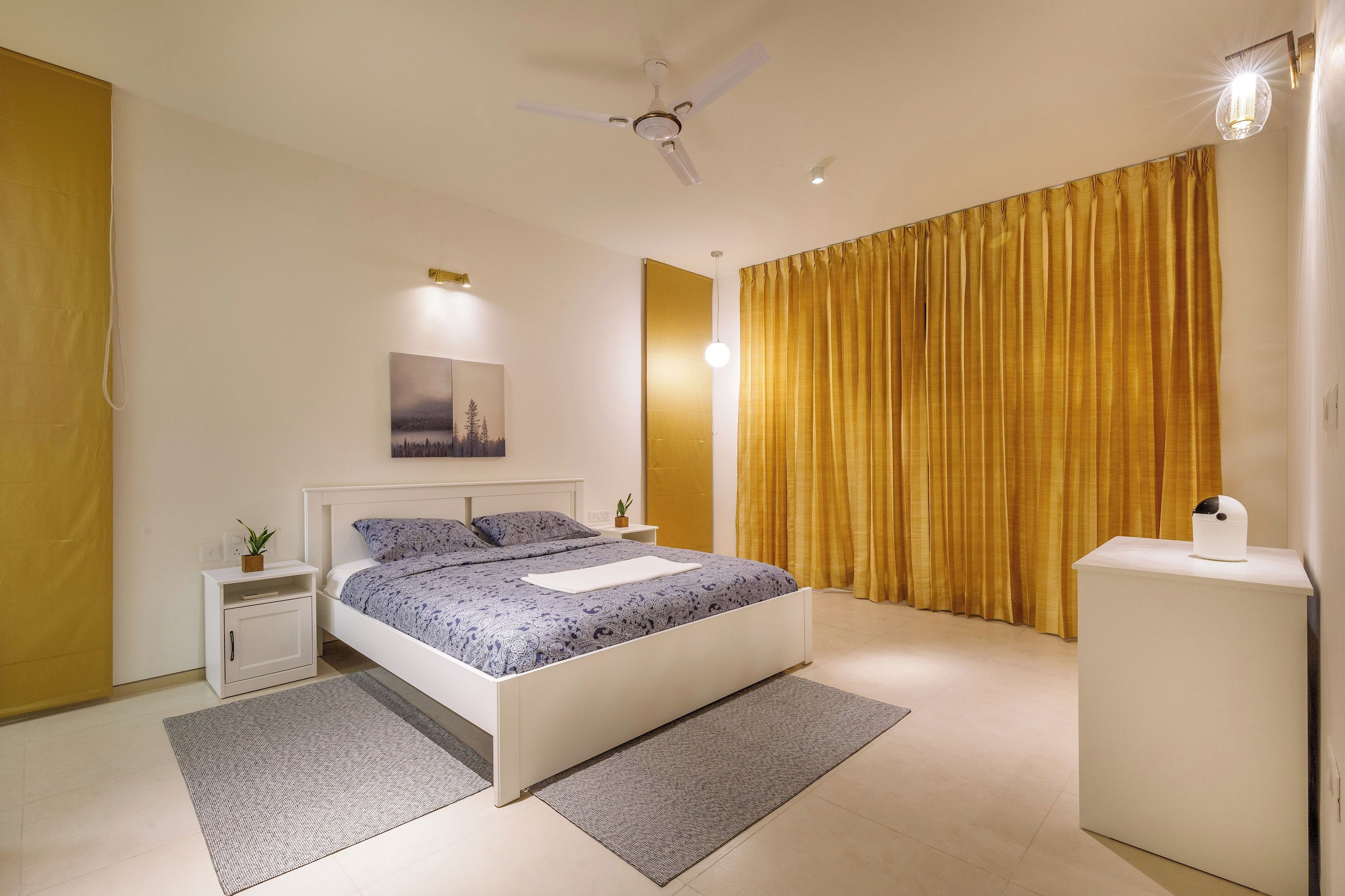 A modern bedroom with a bed, bedside tables, a ceiling fan, and a nightstand with a plant.