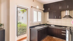 A kitchen with dark cabinets, a black countertop, a window with a view of greenery, and a stainless steel range hood. - Aspire Heights by Red Olive (Bengaluru)