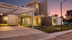A modern house with a covered driveway, a large brick wall, and a well-lit entrance.