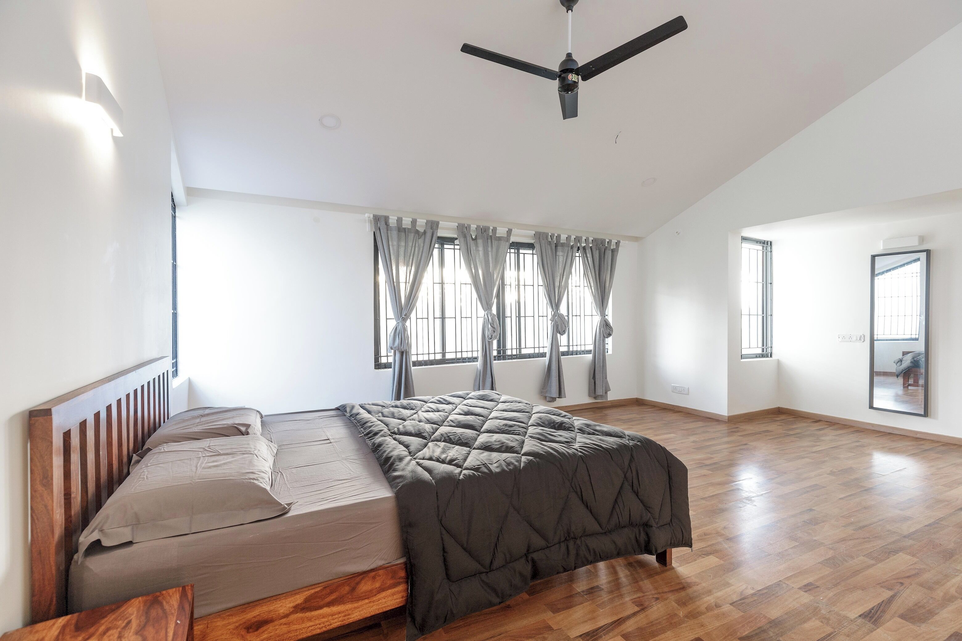 A spacious bedroom with a large bed, a ceiling fan, and large windows with curtains.