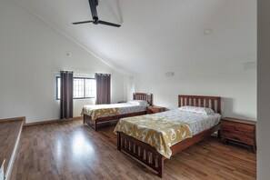 A spacious room with two wooden beds, a ceiling fan, and a large window with curtains.