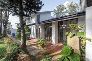 A modern house with a covered patio, a garden with various plants, and a clear sky.