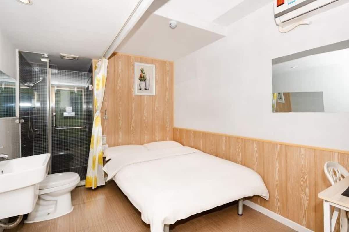 A hotel room with a wooden panel wall, a bed, a shower, and a white sink.