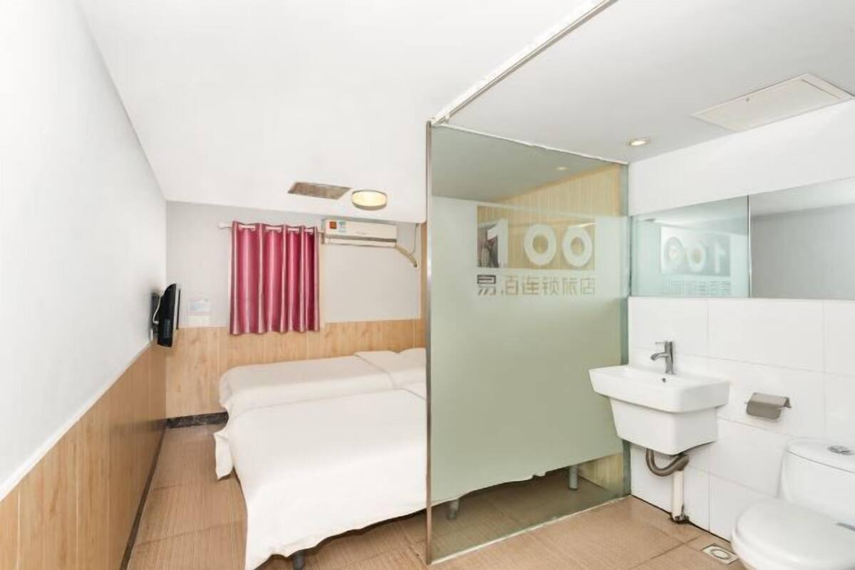 A hotel room with a bed, a bathroom with a sink and toilet, and a glass partition.
