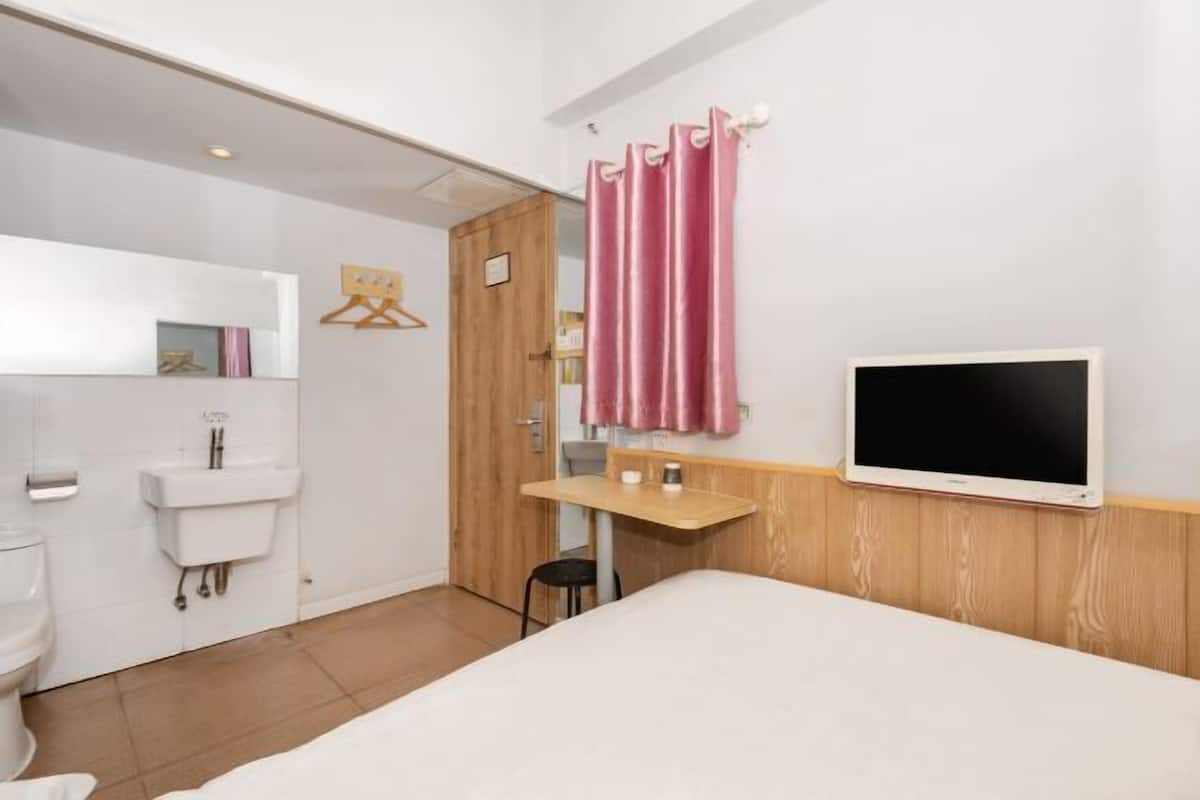 A hotel room with a bed, a desk, a TV, a bathroom with a sink and toilet, and a wooden door.