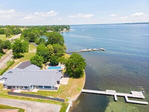 Ein Luftbild eines Sees mit einem Grundstück, einem Steg, einem Schwimmbad und einem Haus mit einer großen Garage.