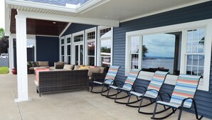 A covered patio with wicker furniture and striped rocking chairs.