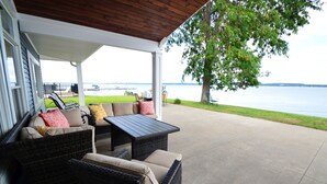 Un patio techado con mobiliario de mimbre, vistas al agua y un área con césped.