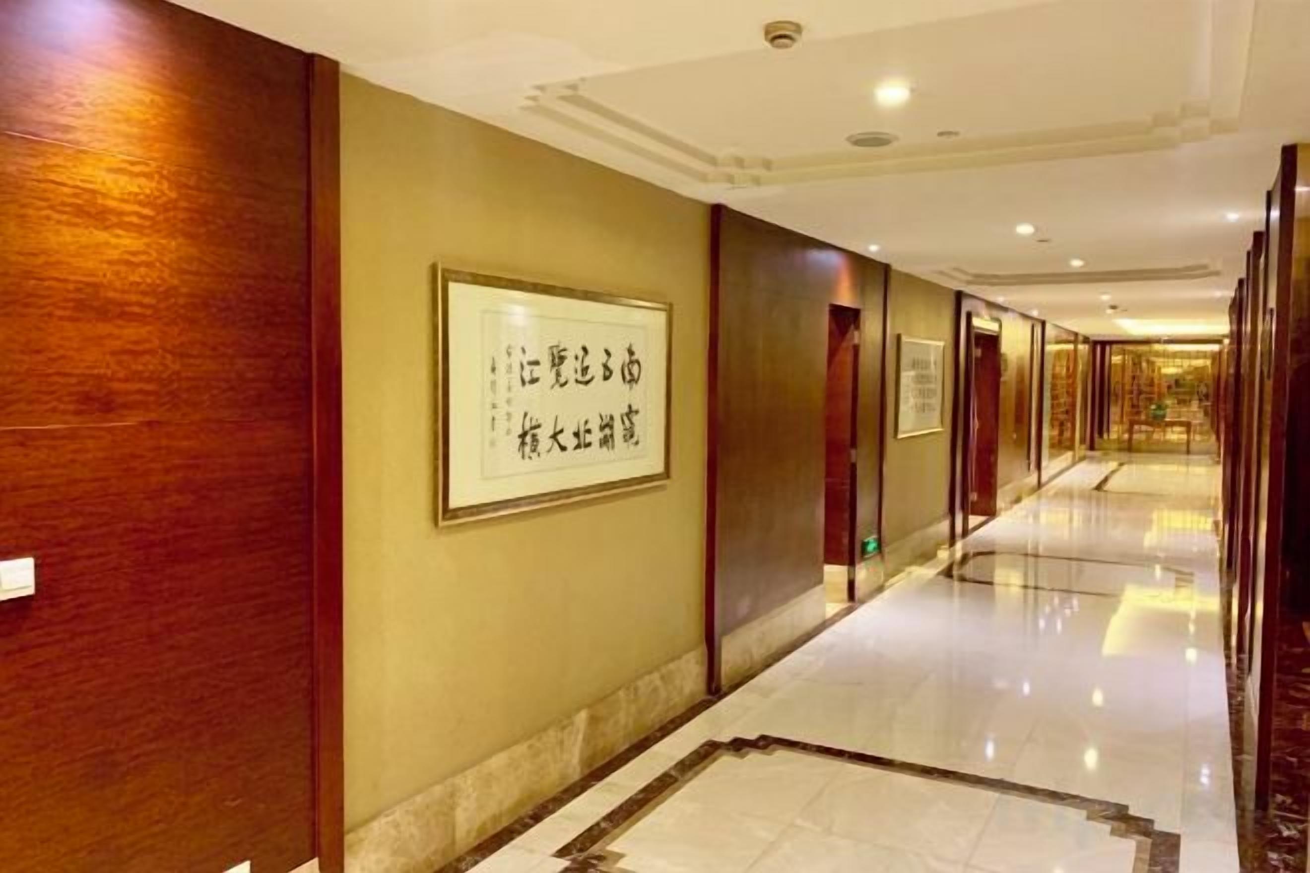 A hotel corridor with framed wall art, polished marble flooring, and wooden paneling.
