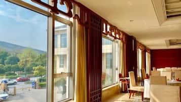 A hotel room with large windows, a view of the outside, and a dining area with tables and chairs.