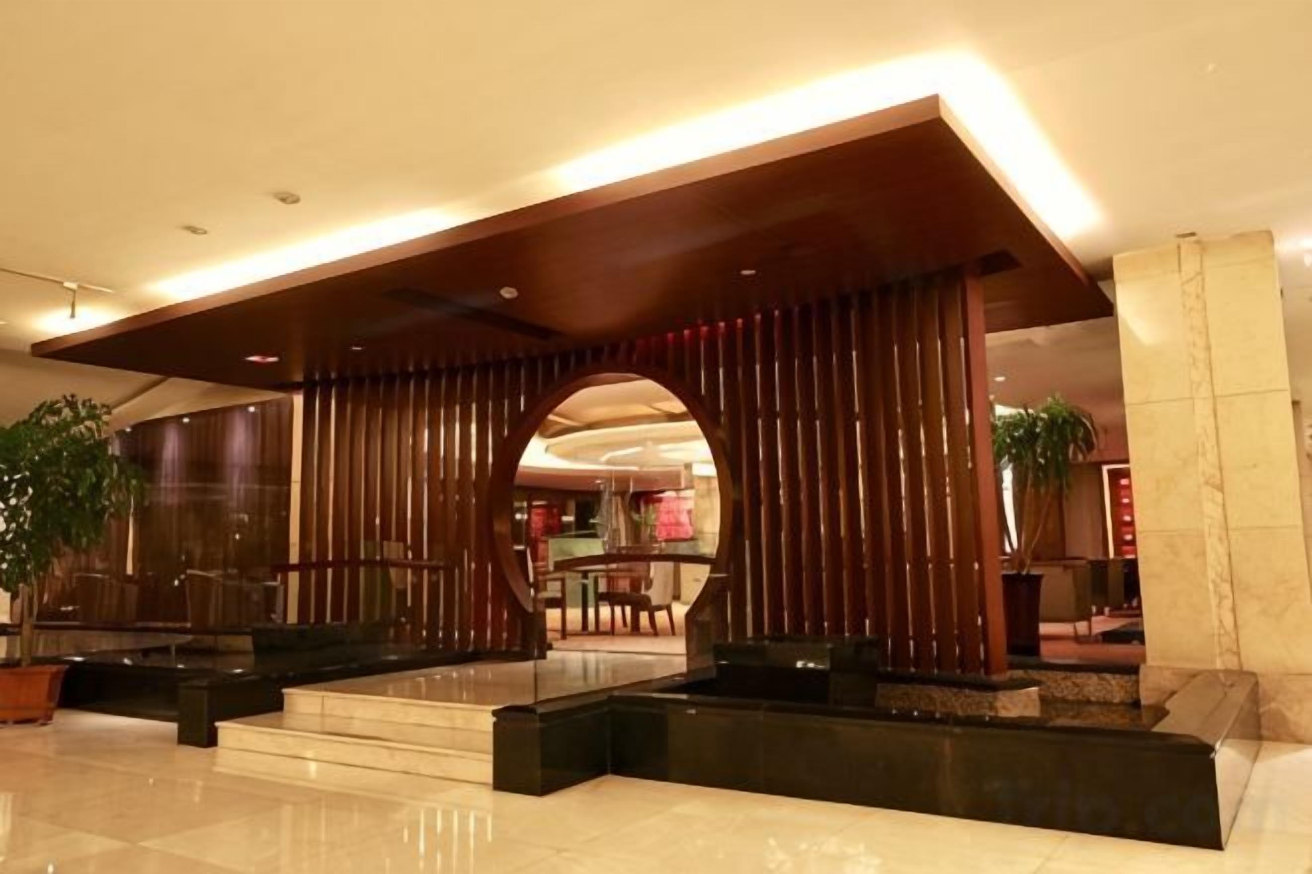 A lobby with a modern design, featuring a reception desk, seating areas, and a large archway.