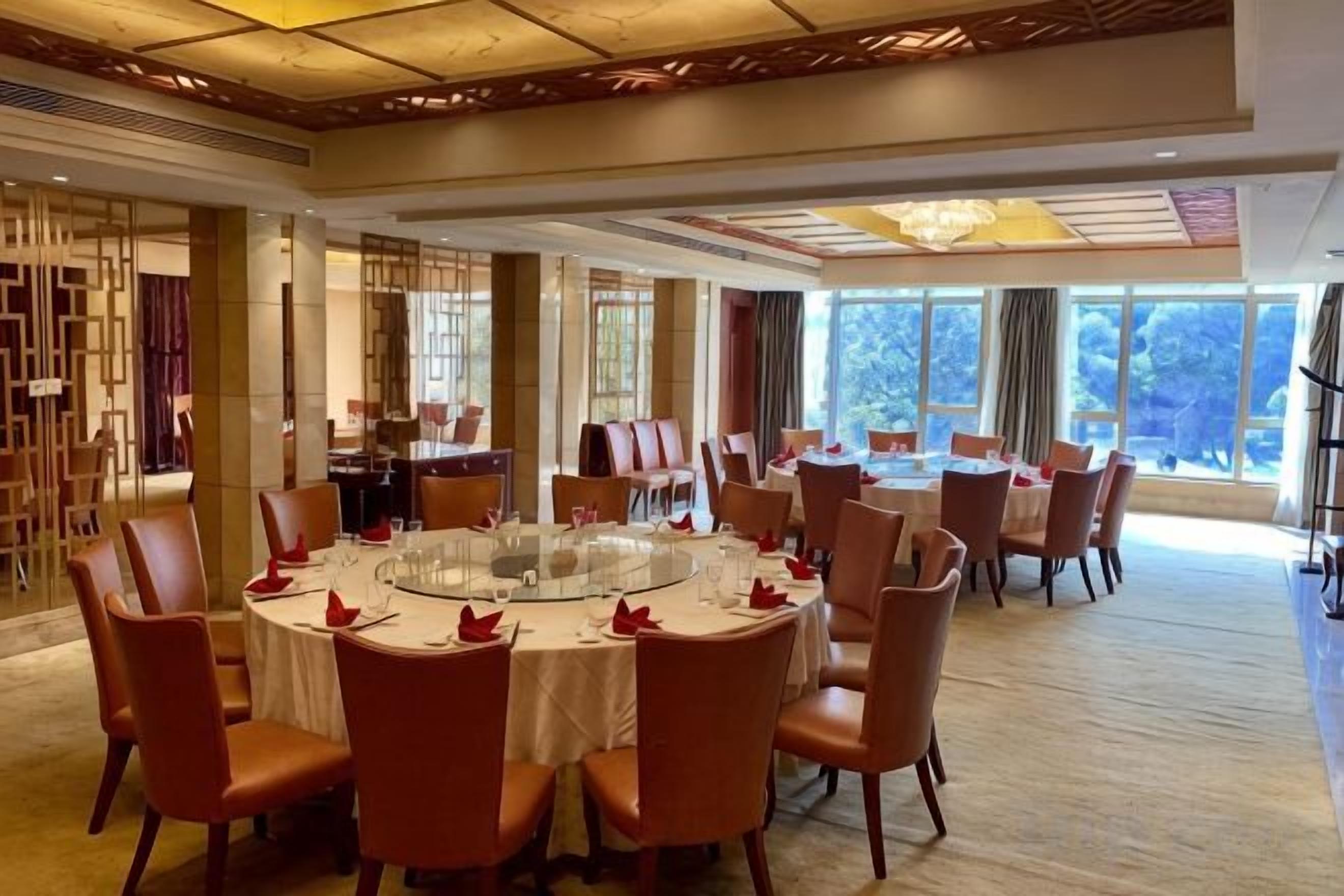 Un comedor con mesas redondas, servilletas rojas y vistas al exterior.