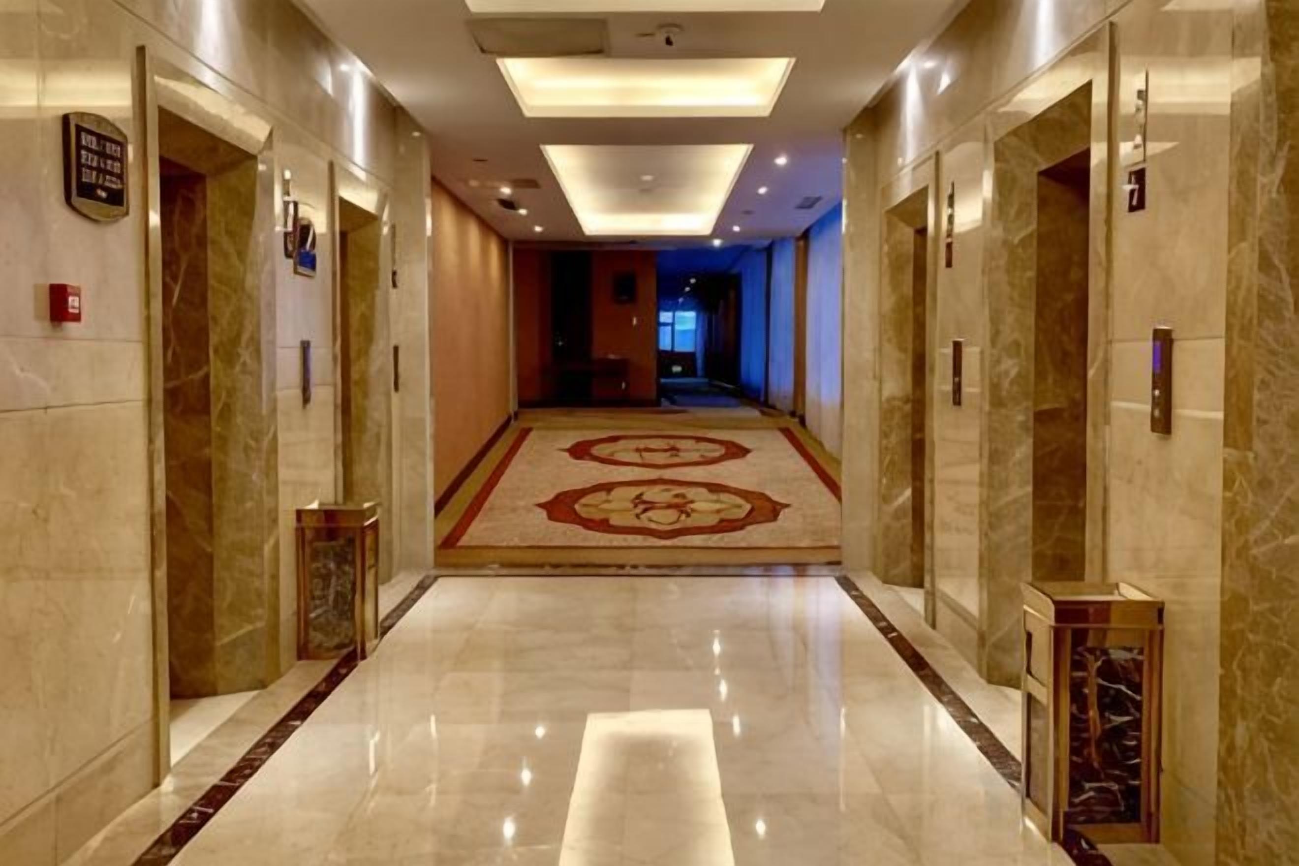 A hotel corridor with marble flooring, a patterned carpet, and doors with numbered signs.