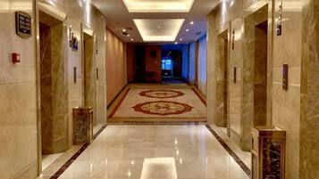 A hotel corridor with marble flooring, a patterned carpet, and doors with numbered signs.
