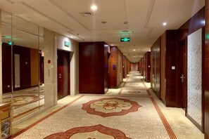 En hotellkorridor med ett mönstrat golv, spegelbeklädda väggar och dörrar som leder till rummen.